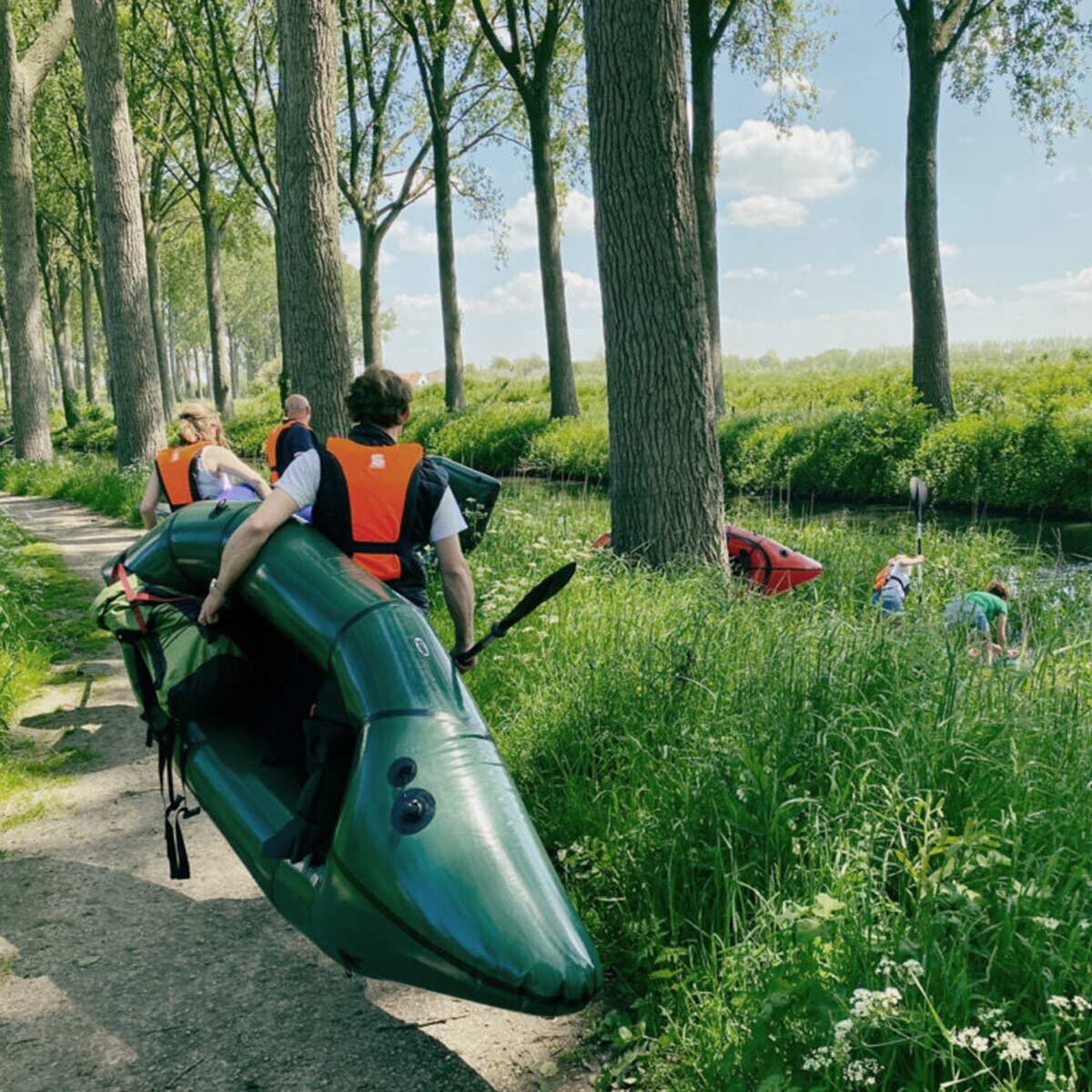 Group carrying a packraft along a tree-lined lane in the polder near Het Zwin.