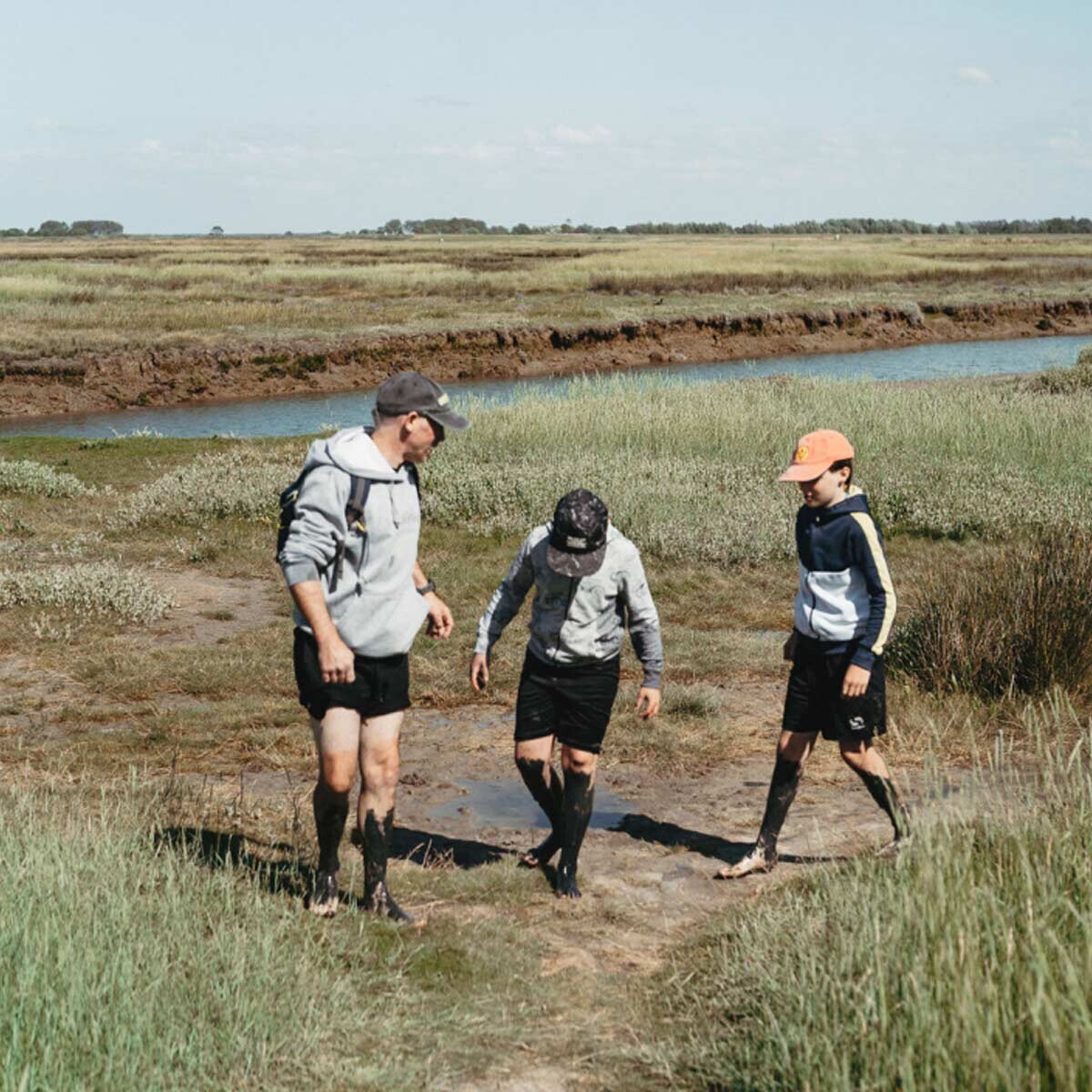 Hikers walking barefoot through the mudflats of Het Zwin nature reserve.