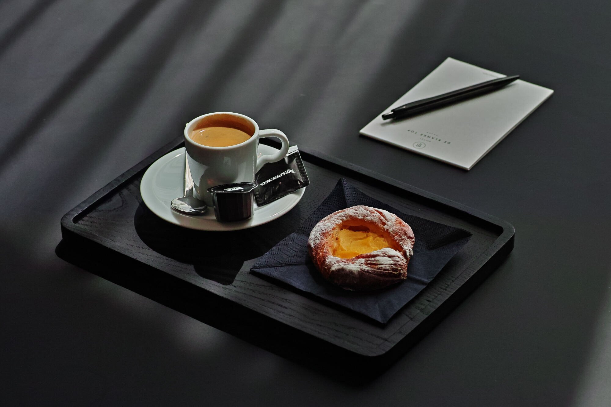 Espresso and pastry on a tray with a notepad in the meeting room.